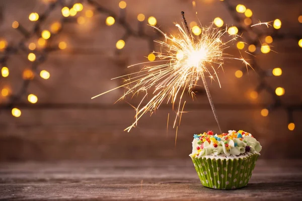 Cupcake with sparkler on old wooden background — Stock Photo, Image