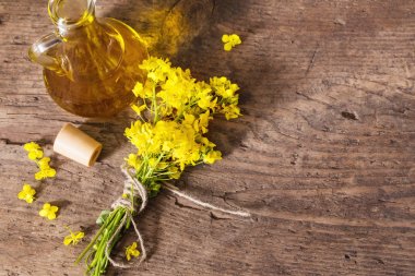 rapeseed oil (canola) and rape flowers on wooden table clipart
