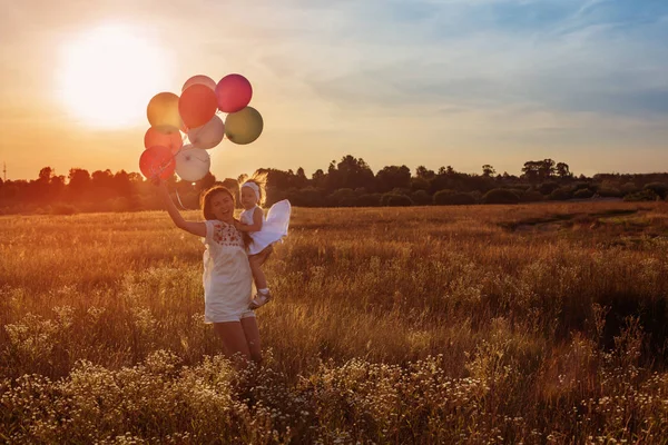Glückliche Mutter und Tochter mit Luftballons bei Sonnenuntergang — Stockfoto