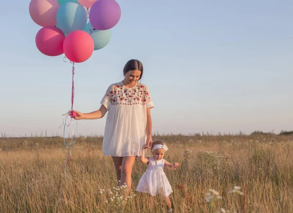 Glückliche Mutter und Tochter mit Luftballons bei Sonnenuntergang — Stockfoto