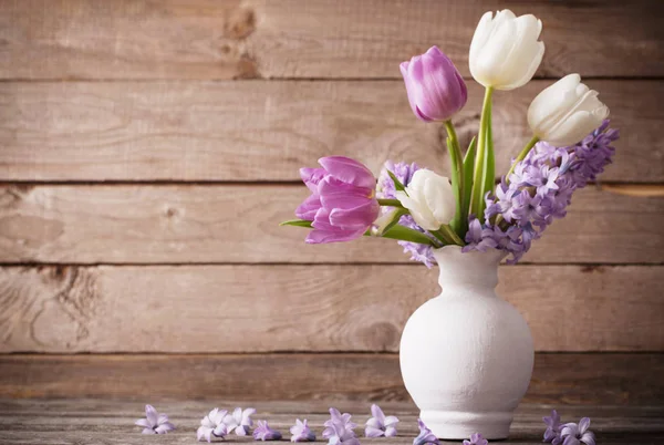 Spring flowers in vase on old wooden background — Stock Photo, Image