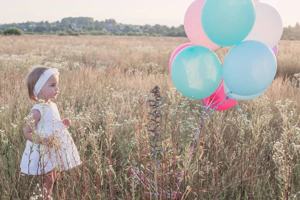 Liten flicka i vit klänning med ballonger utomhus — Stockfoto