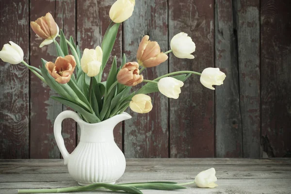 Tulips in glass vase on old wooden background — Stock Photo, Image
