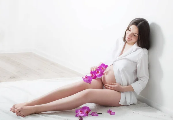 Mulheres grávidas com orquídeas em fundo branco — Fotografia de Stock