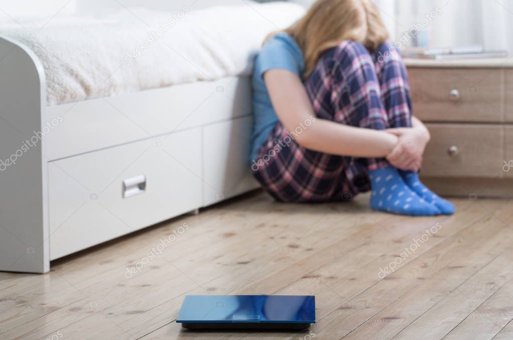 sad teenager girl with scales on floor