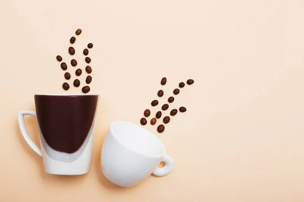 Koffiebonen en een twee kopjes op een lichte achtergrond — Stockfoto