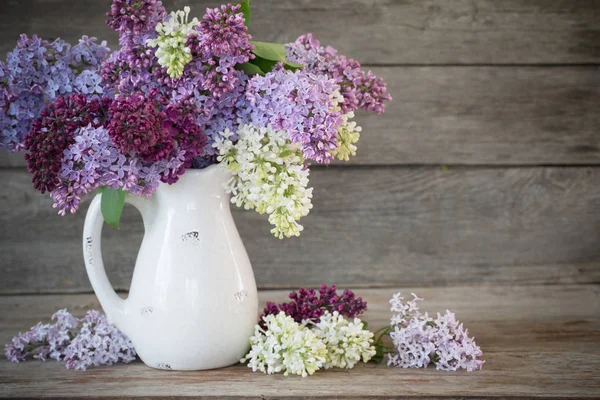 Lilac in jug on old wooden background — Stock Photo, Image