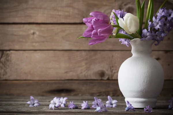 Spring flowers in vase on old wooden background — Stock Photo, Image