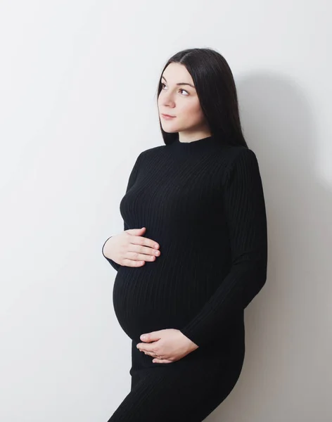 Беременные женщины в черном платье на фоне белой стены — стоковое фото