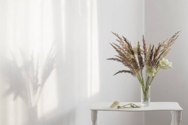 Beyaz iç güneş ışığında cam vazo yabani çim bitkiler