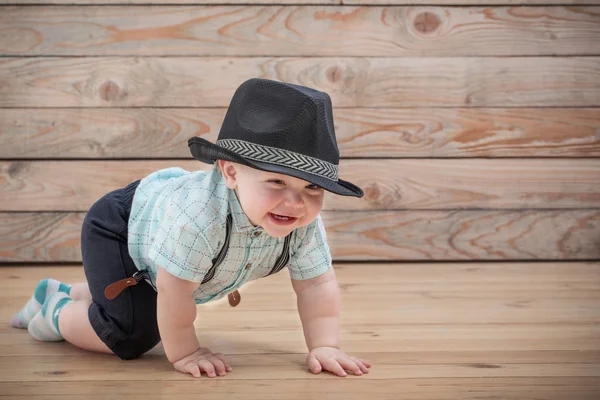 黒の帽子の赤ちゃんシャツとサスペンダーのショートパンツの木の背もたれ — ストック写真