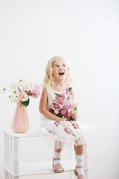 Mooie kleine blonde meisjes met bloemen op witte achtergrond — Stockfoto