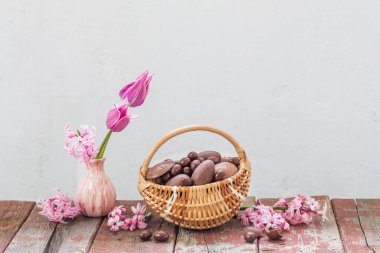 Sepette paskalya çikolatası ve eski ahşap üzerinde pembe çiçekler.