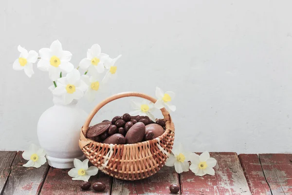 Pisanki czekoladowe w koszyku i wiosenne kwiaty na starym drewnianym — Zdjęcie stockowe