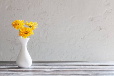 ahşap masa üzerinde beyaz vazo sarı zinnia 