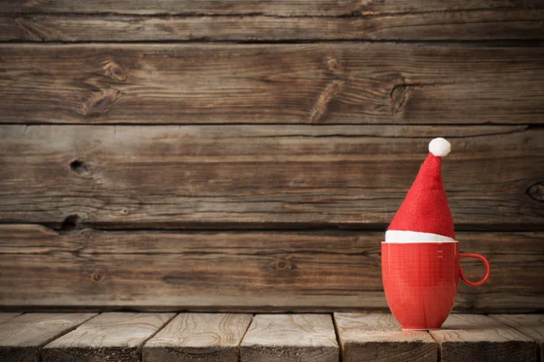 Смішна червона чашка в капелюсі Санта на старому темному дерев'яному фоні — стокове фото