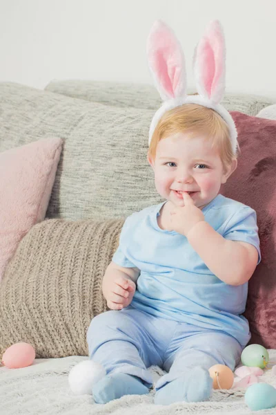 Beau petit garçon dans les oreilles de lapin avec des œufs de Pâques sur le canapé — Photo