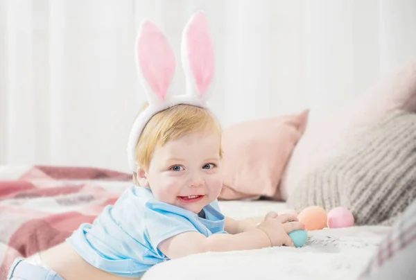 Όμορφο μικρό αγόρι σε αυτιά κουνελιού με πασχαλινά αυγά στον καναπέ — Φωτογραφία Αρχείου