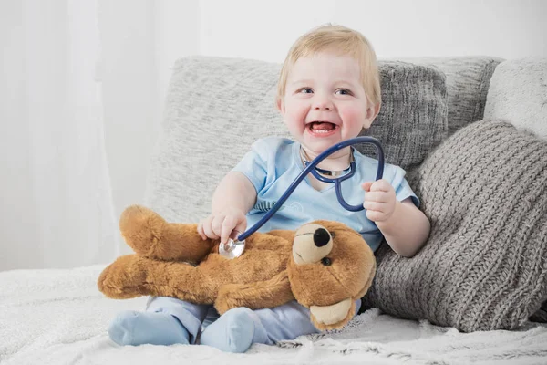 Little child plays doctor with teddy bear at home — Stock Photo, Image