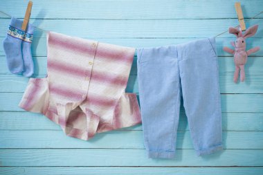 Bebek kıyafetleri ahşap arka planda ipte sallanıyor.