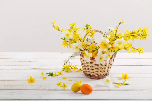 Húsvéti tojás tavaszi virágokkal fehér fa asztalon — Stock Fotó