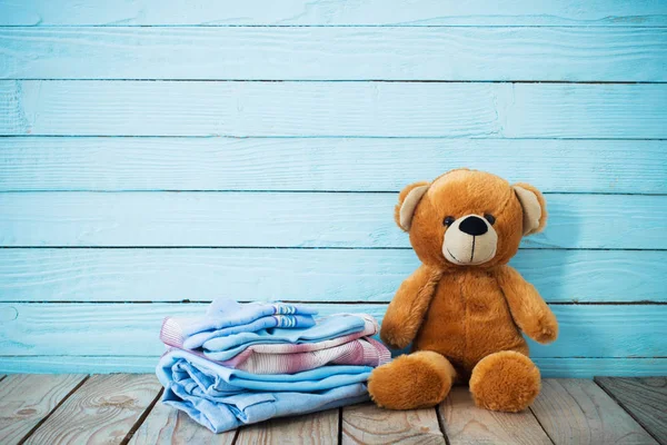 Ubrania dla niemowląt i niedźwiedź zabawki na starym drewnianym tle — Zdjęcie stockowe