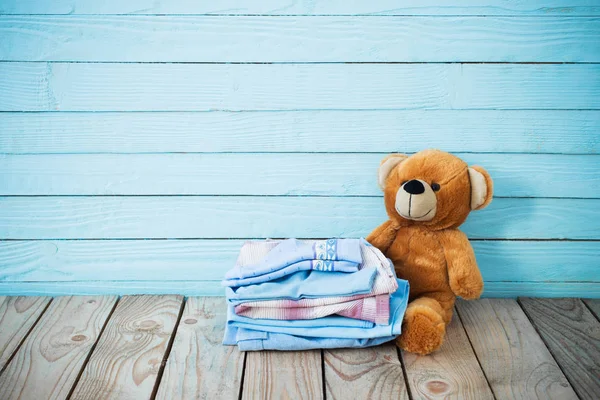 Vestiti per bambini e orso giocattolo su sfondo di legno vecchio — Foto Stock