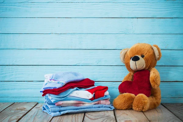 Ropa de bebé y oso de juguete sobre fondo de madera viejo — Foto de Stock