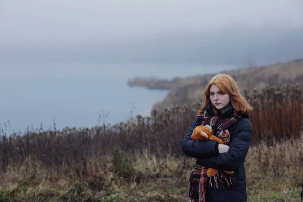Ragazza adolescente bionda triste che abbraccia orsacchiotto dal lago nebbioso. C — Foto Stock
