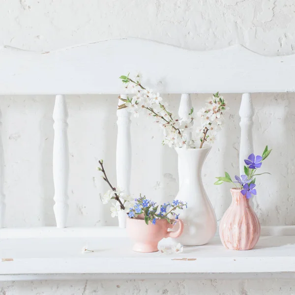 Copos e vasos com flores de primavera na prateleira branca de madeira vintage — Fotografia de Stock