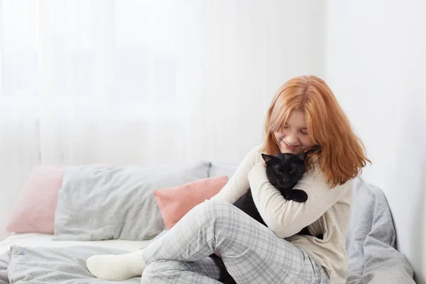 Bela adolescente menina com gato preto na cama em casa — Fotografia de Stock