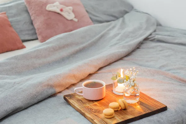 Herbal tea with macaroons and candles on wooden tray on bed — 스톡 사진