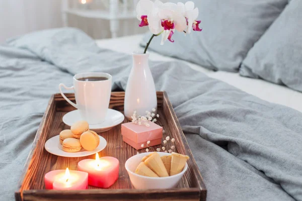 Kaffe, godis, ljus, blommor och gördel på träbricka i sängen — Stockfoto
