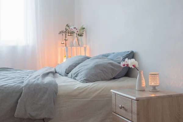 Orched flowers  in vase and burning candles in white bedroom — 스톡 사진