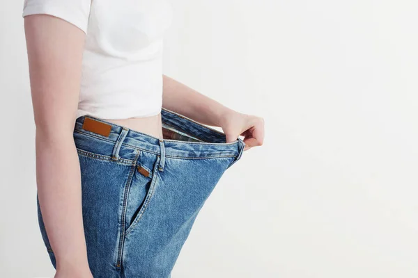 Chica tirando de sus pantalones vaqueros grandes y mostrando la pérdida de peso — Foto de Stock