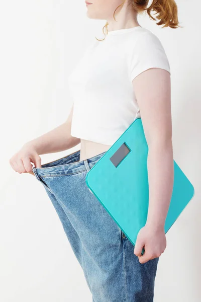 Girl with scale pulling her big jeans and showing weight loss — 스톡 사진
