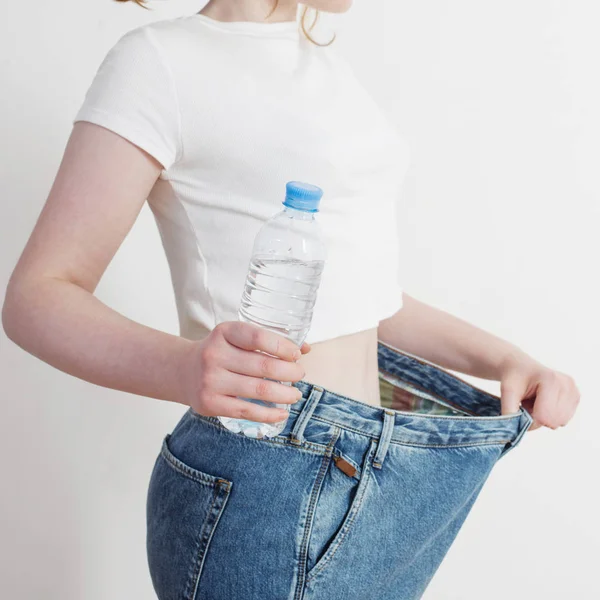 Girl with water in bottle pulling her big jeans and showing weig — 스톡 사진