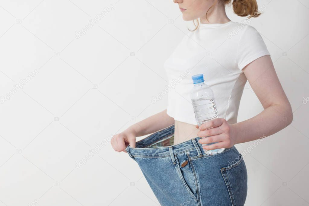 girl with water in bottle pulling her big jeans and showing weig