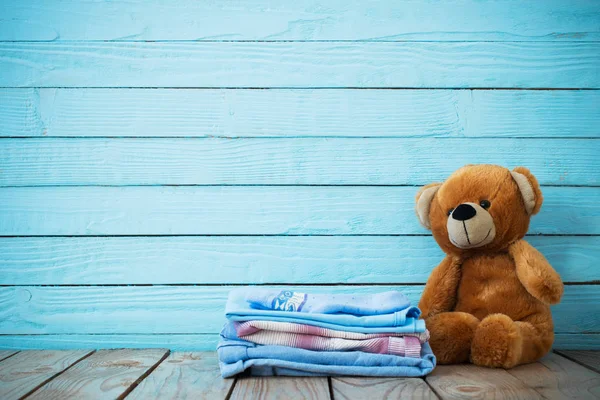 Детская одежда и игрушечный медведь на старом деревянном фоне — стоковое фото