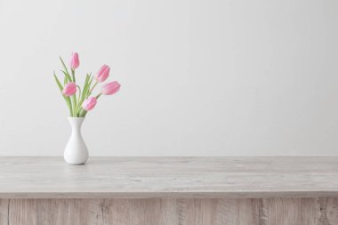 Beyaz seramik vazoda pembe laleler arka plandaki ahşap masada. 