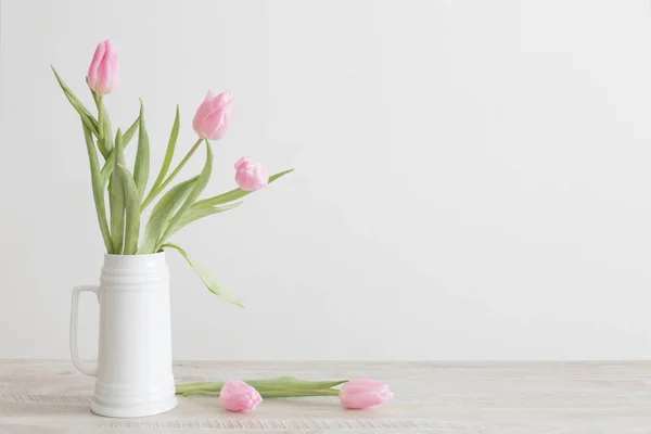 Pink tulips in white ceramic jug on wooden table on background w — 스톡 사진