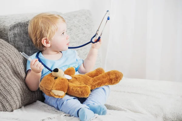 little child plays doctor with teddy bear at home