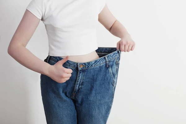 Дівчина тягне великі джинси і показує втрату ваги — стокове фото