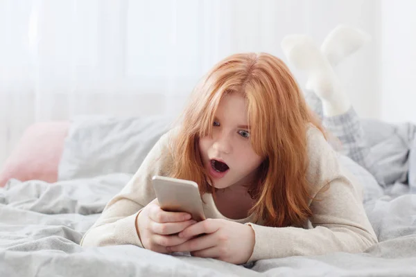 Tonårstjej med smartphone i sängen — Stockfoto