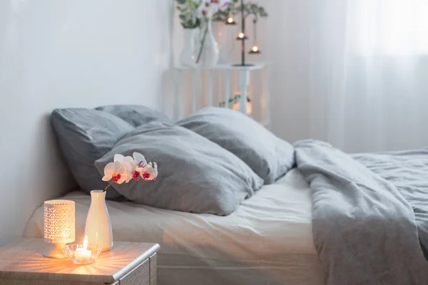 Orched bloemen in vaas en brandende kaarsen in witte slaapkamer — Stockfoto