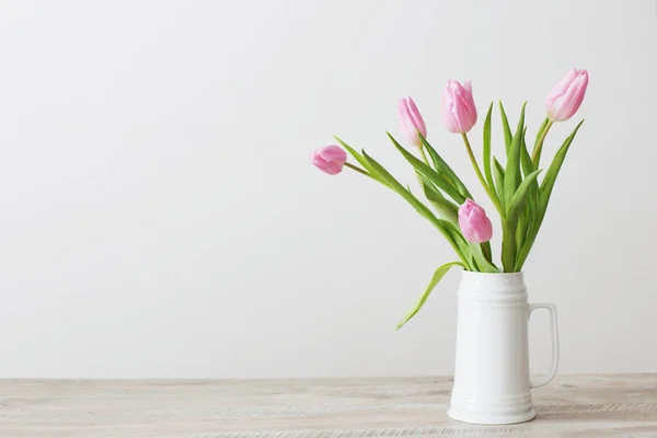 Pink tulips in white ceramic jug on wooden table on background w — Stock Photo, Image