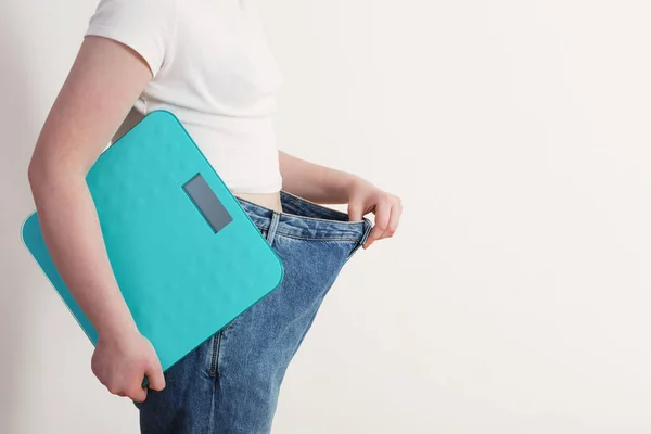 Chica con escala tirando de sus grandes pantalones vaqueros y mostrando la pérdida de peso —  Fotos de Stock