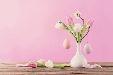 Paskalya yumurtaları ve laleler pembe arka planda vazoda. 