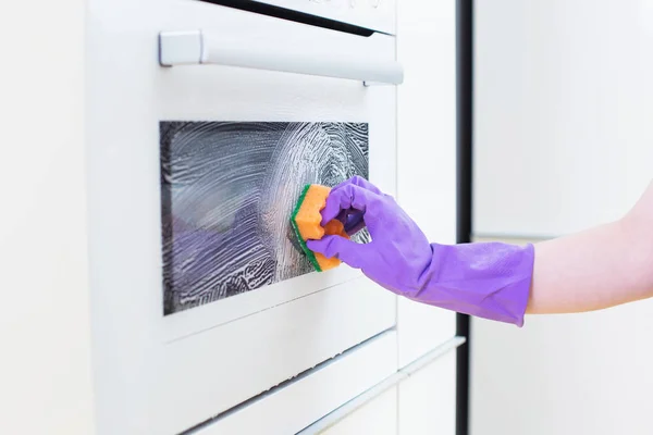 Vrouwelijke hand in paarse handschoen sponzen oven in de keuken — Stockfoto