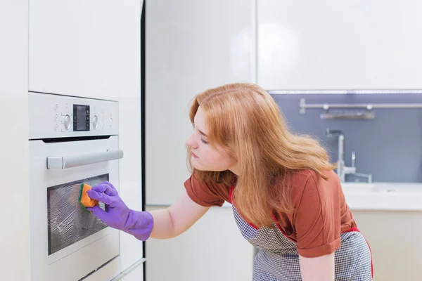 Meisje in paarse handschoenen sponzen oven in moderne keuken — Stockfoto